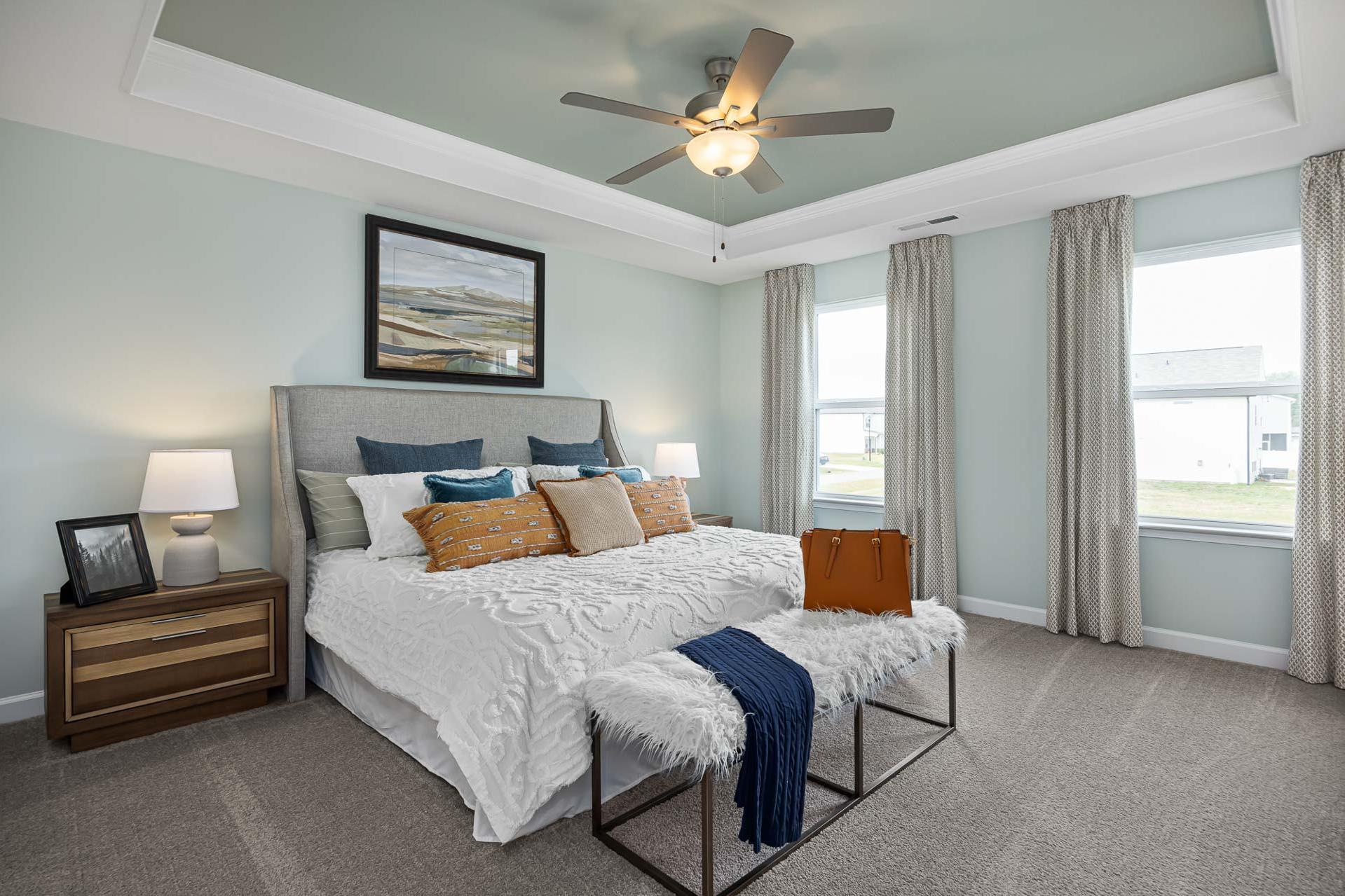 Serene master bedroom at Beverly Place in Four Oaks NC featuring king bed, ceiling fan, and large windows by Davidson Homes
