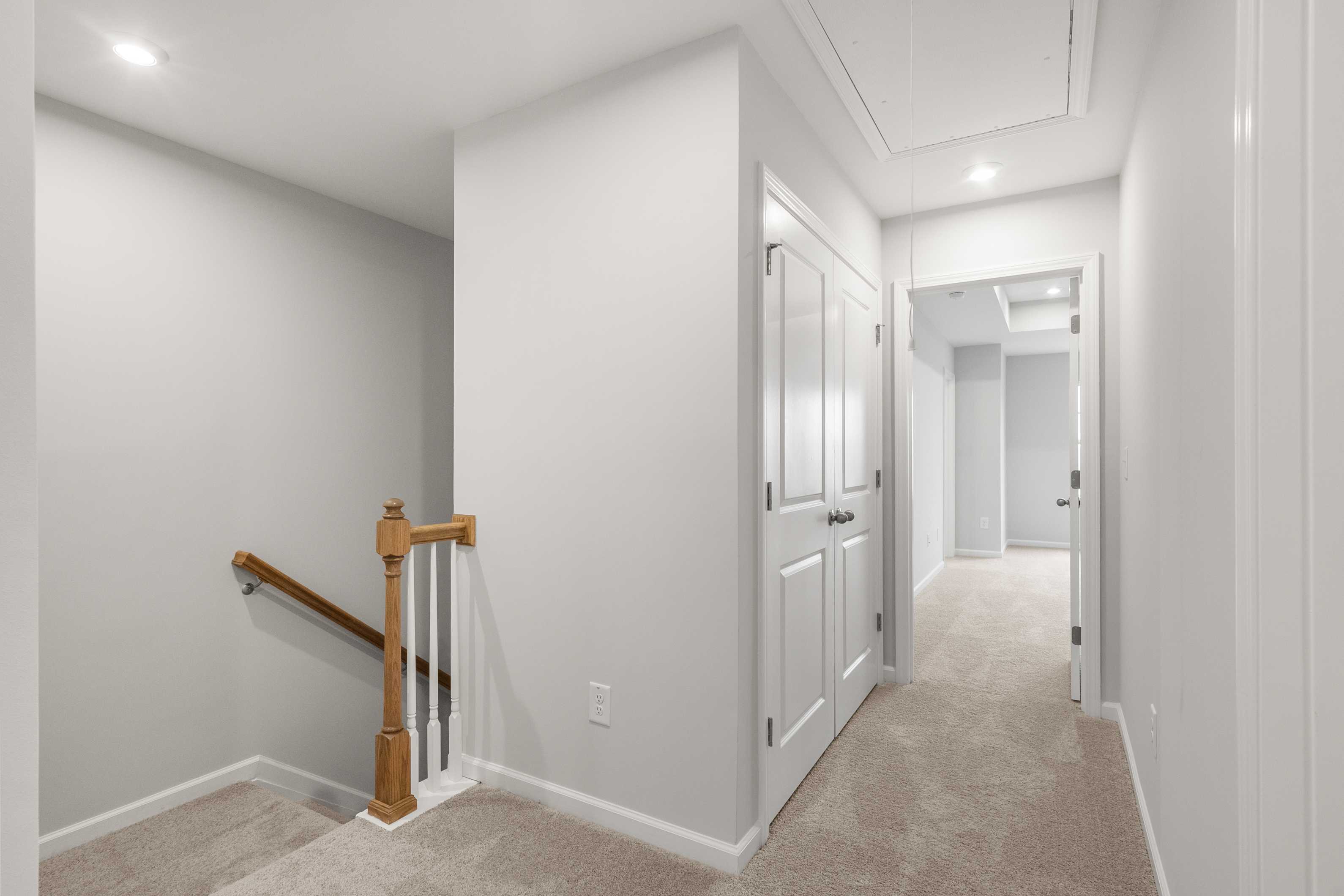 Upper floor hallway in The Durant A home featuring wooden staircase, beige carpet, white walls, and double closet doors