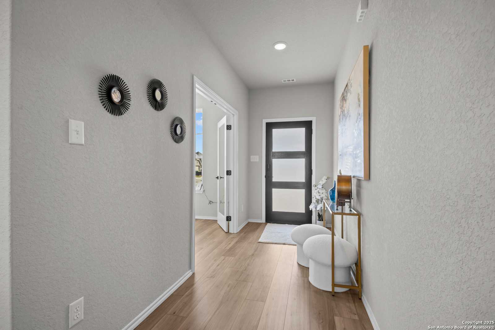 Elegant hallway with gray walls, hardwood floors, frosted glass front door, and modern decor in Davidson Homes The Douglas B, Converse, Texas