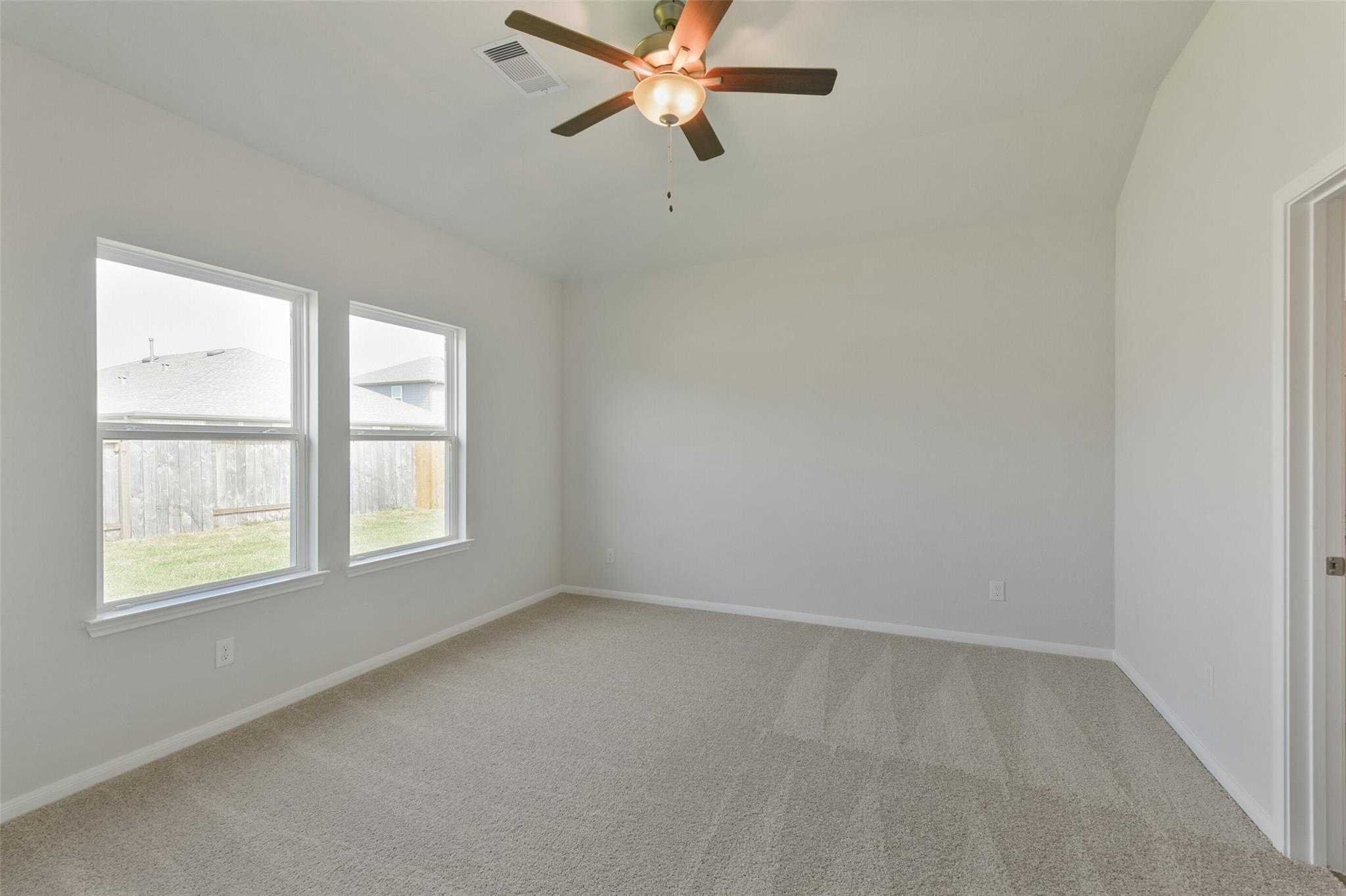Spacious secondary bedroom with beige carpet, ceiling fan, and large windows overlooking fenced backyard in Davidson Homes The Laguna B, Dayton, Texas