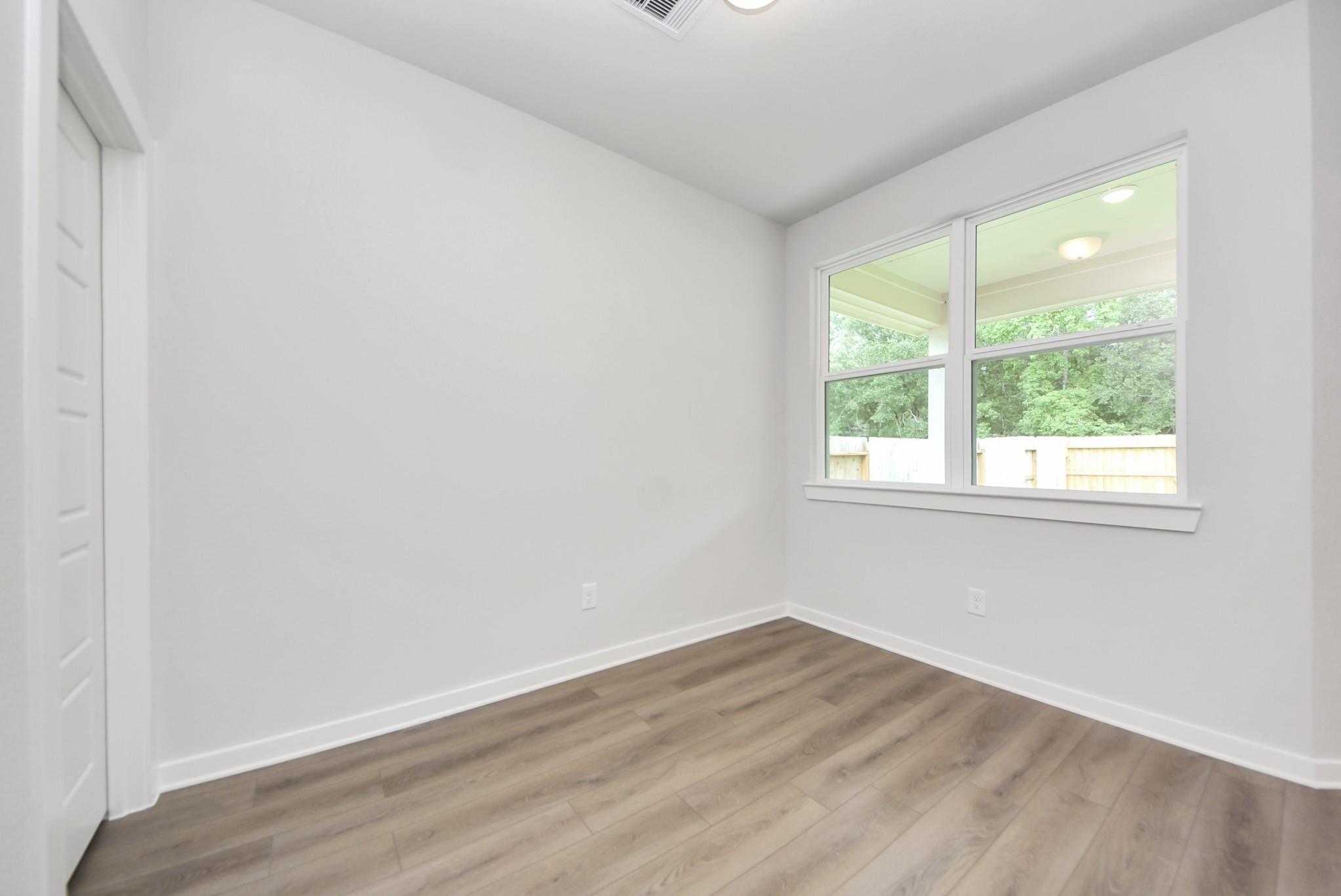 Bright, neutral bedroom with wood-look flooring in The Daphne F floor plan at Sundance Cove in Crosby, Texas.