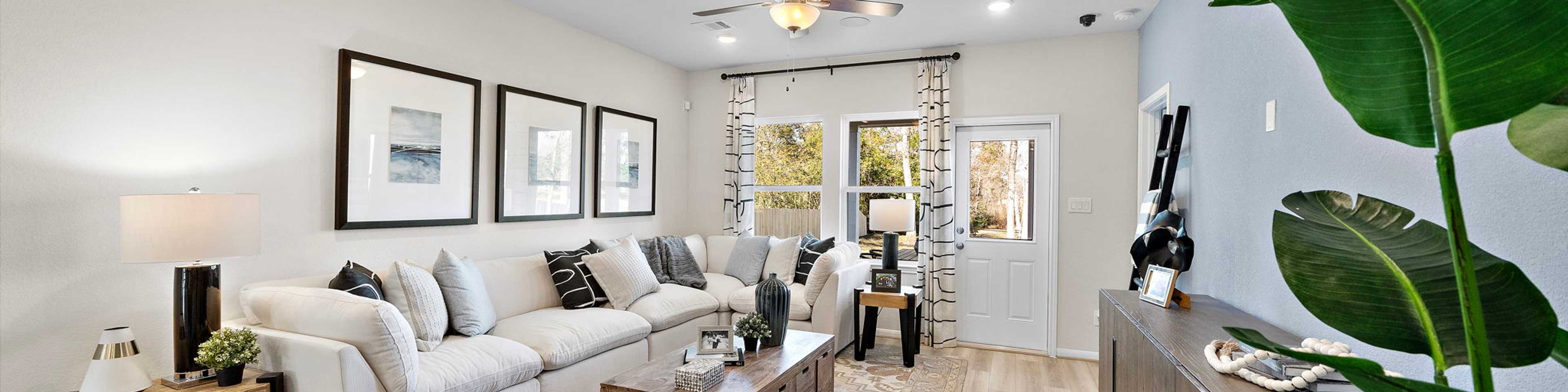 Modern open-concept living room at The Villages at WestPointe in Dayton Texas with white sectional sofa hardwood floors ceiling fan and potted plants