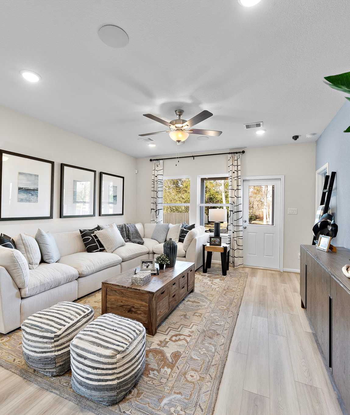 Modern open-concept living room at The Villages at WestPointe in Dayton Texas with white sectional sofa hardwood floors ceiling fan and potted plants