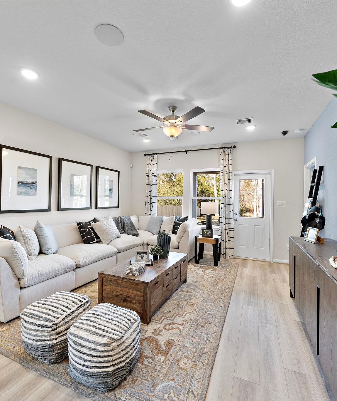 Modern open-concept living room at The Villages at WestPointe in Dayton Texas with white sectional sofa hardwood floors ceiling fan and potted plants