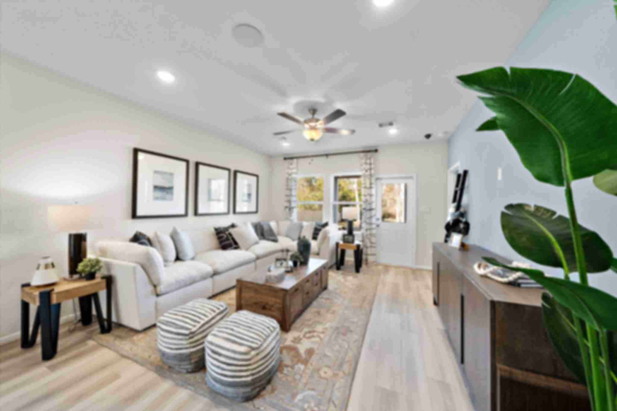 Modern open-concept living room at The Villages at WestPointe in Dayton Texas with white sectional sofa hardwood floors ceiling fan and potted plants
