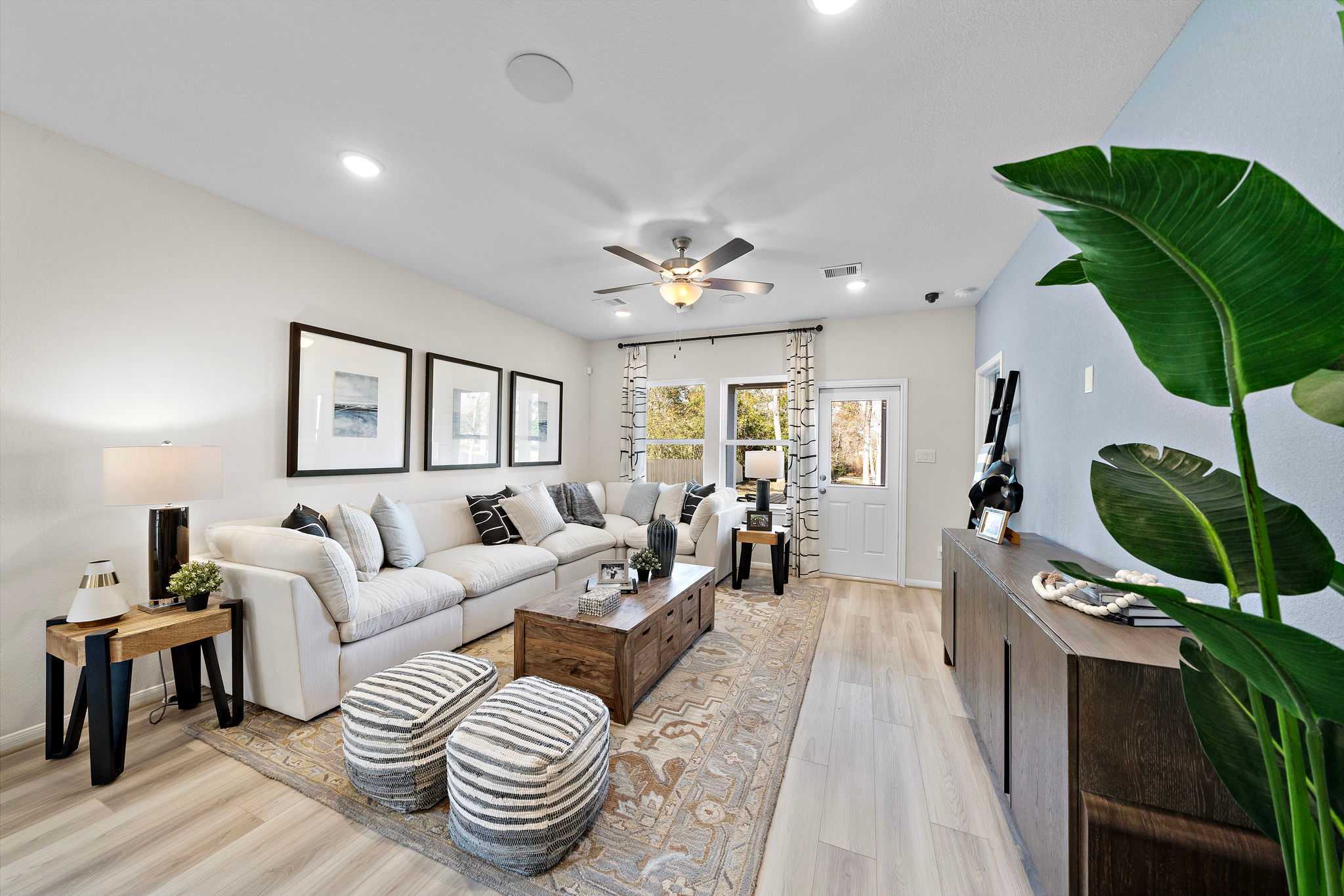 Modern open-concept living room at The Villages at WestPointe in Dayton Texas with white sectional sofa hardwood floors ceiling fan and potted plants