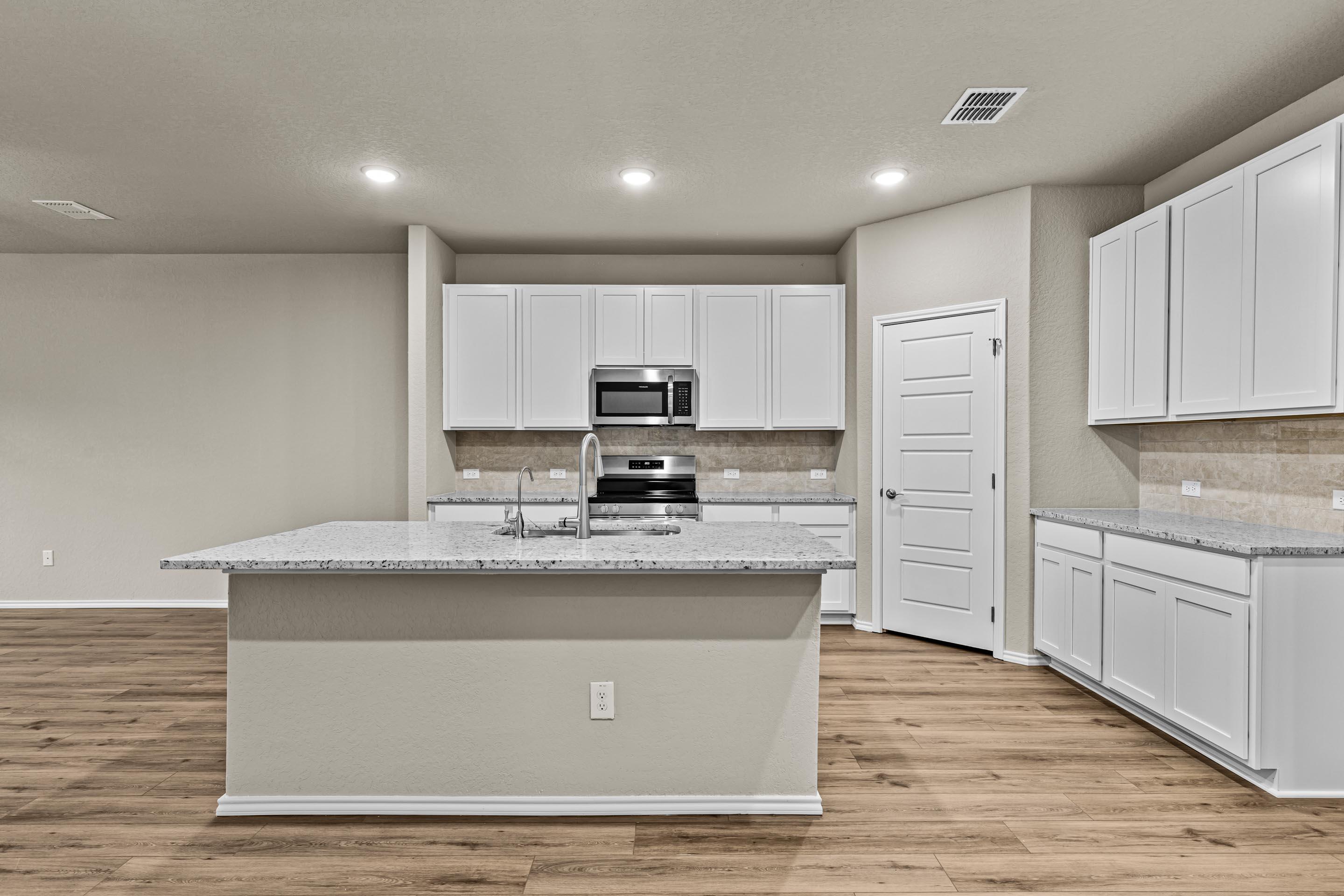 Modern kitchen with white cabinets, granite island, stainless appliances in Davidson Homes The Douglas F, San Antonio, Texas