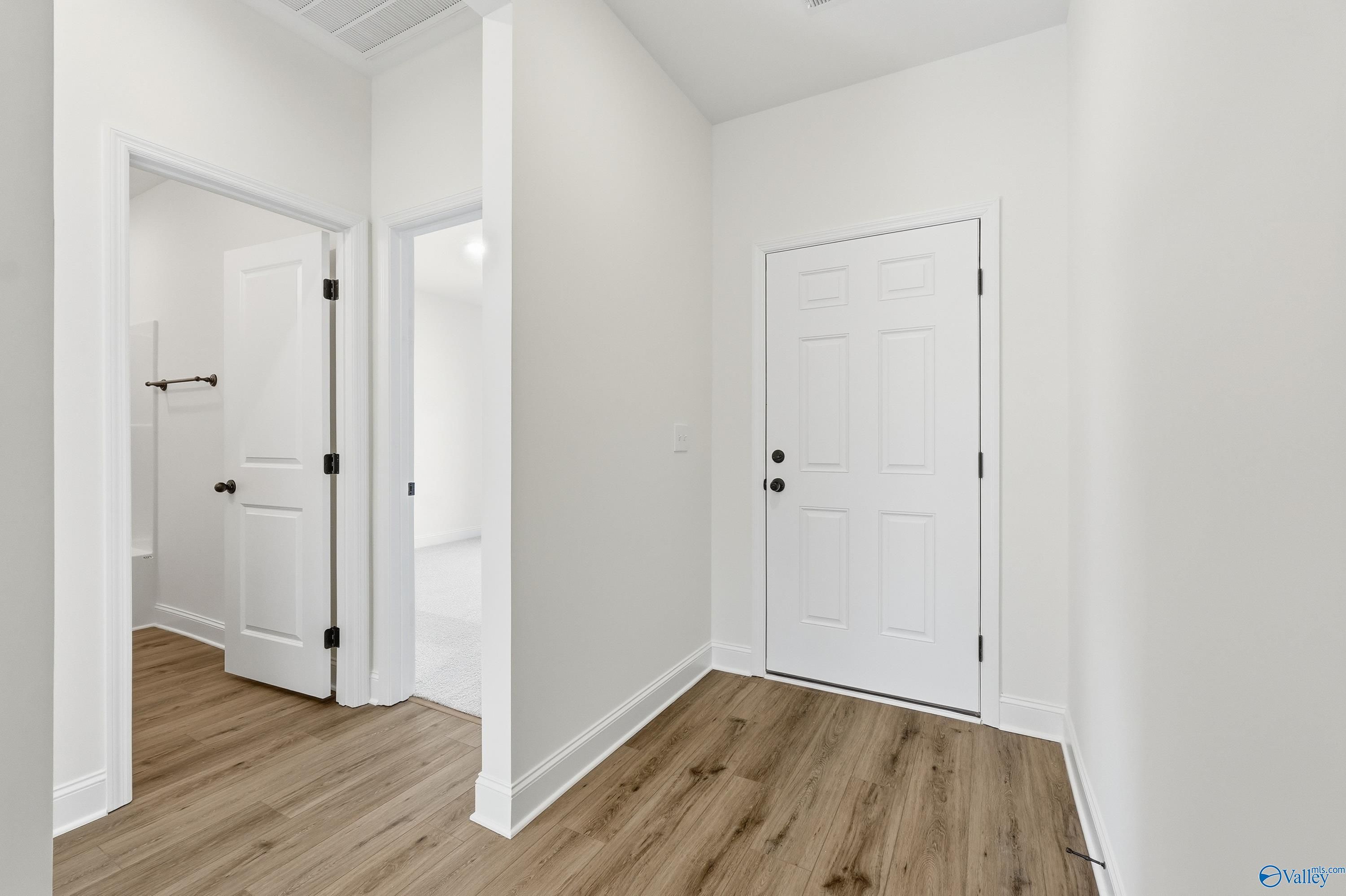 Bright hallway with white paneled doors, open bathroom entry, and hardwood floors in Davidson Homes The Franklin C, New Market, AL