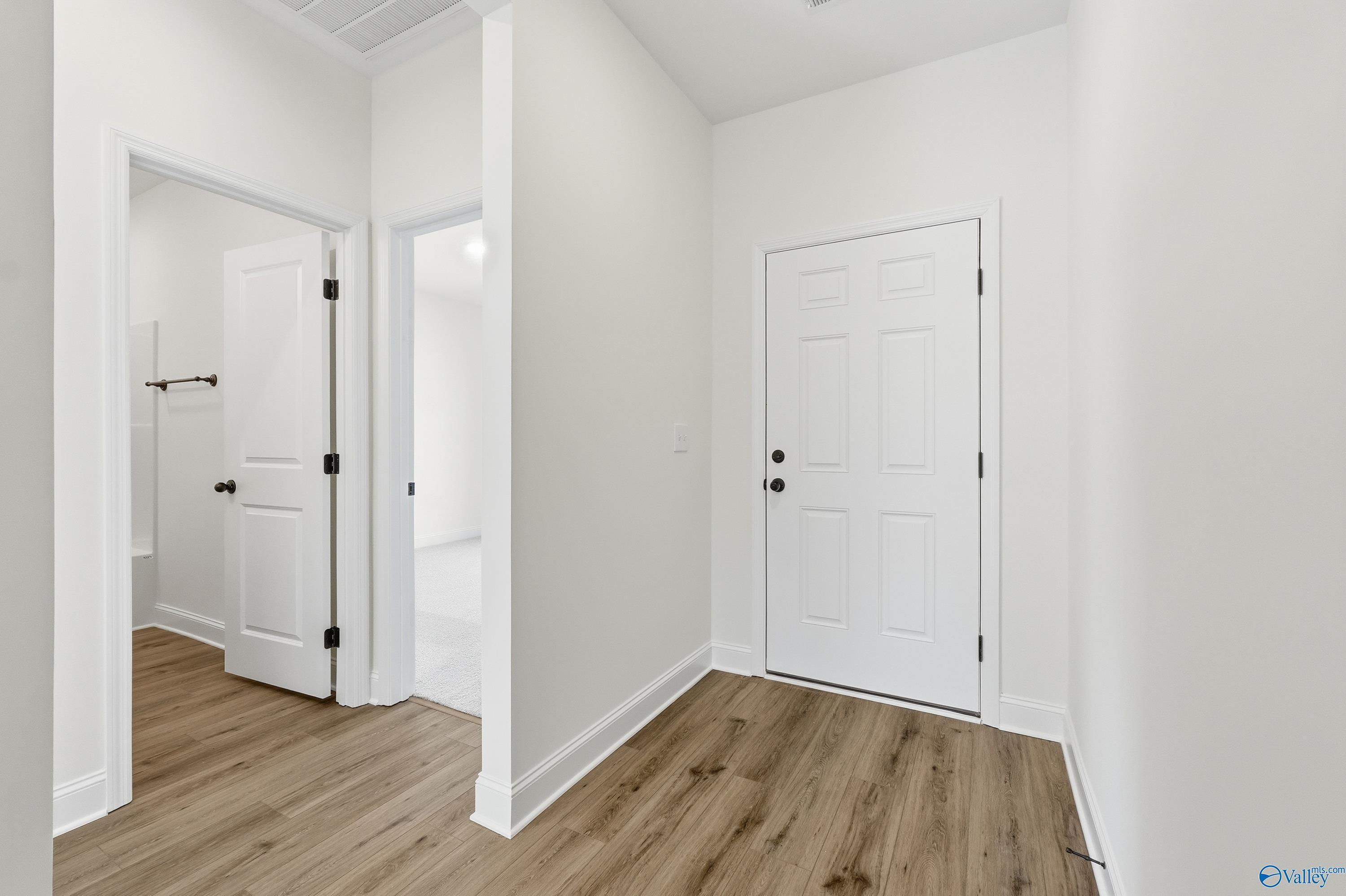 Bright hallway with white paneled doors, open bathroom entry, and hardwood floors in Davidson Homes The Franklin C, New Market, AL