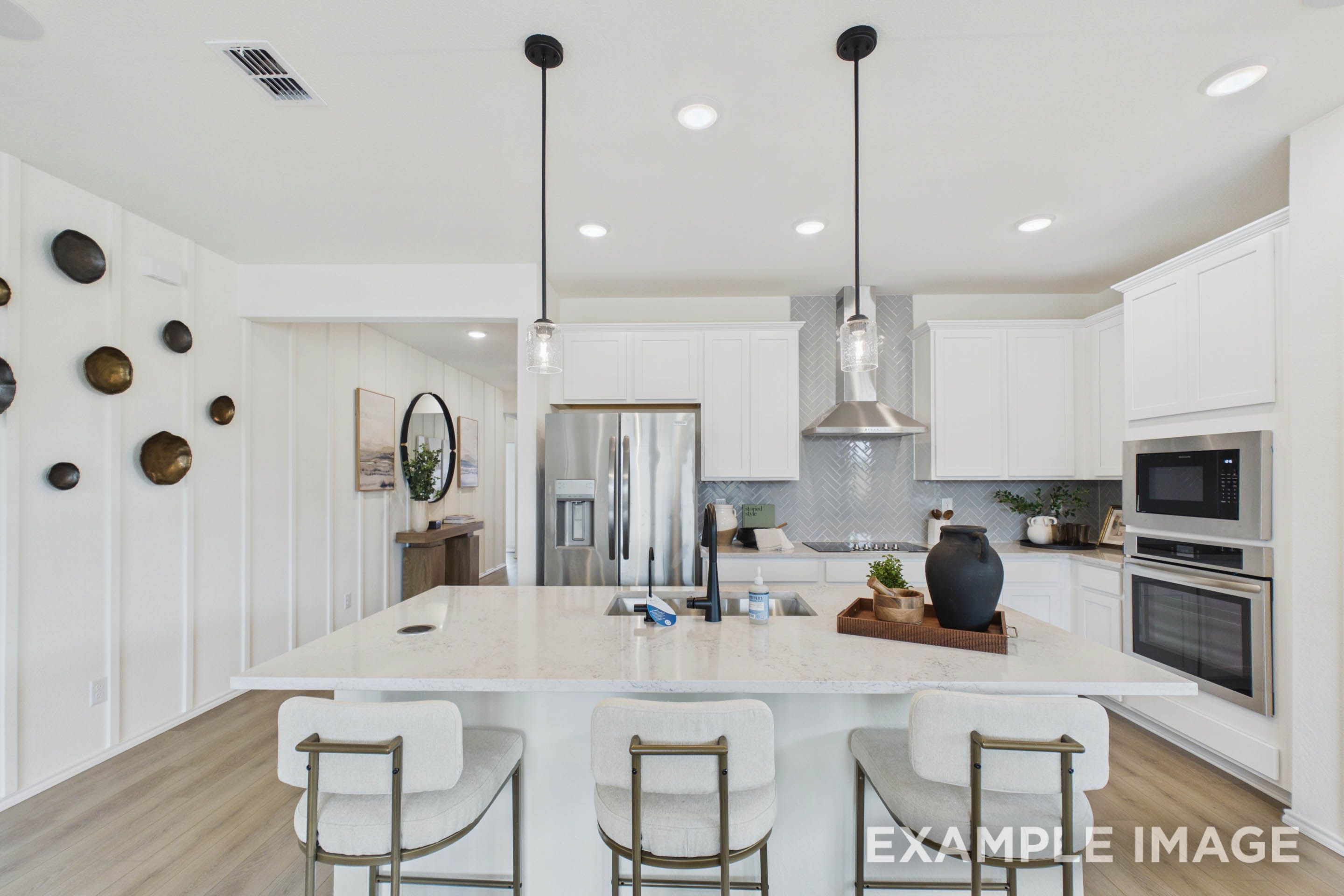 Modern kitchen in The Laurel G featuring a spacious quartz island, white cabinetry, and a herringbone tile backsplash.