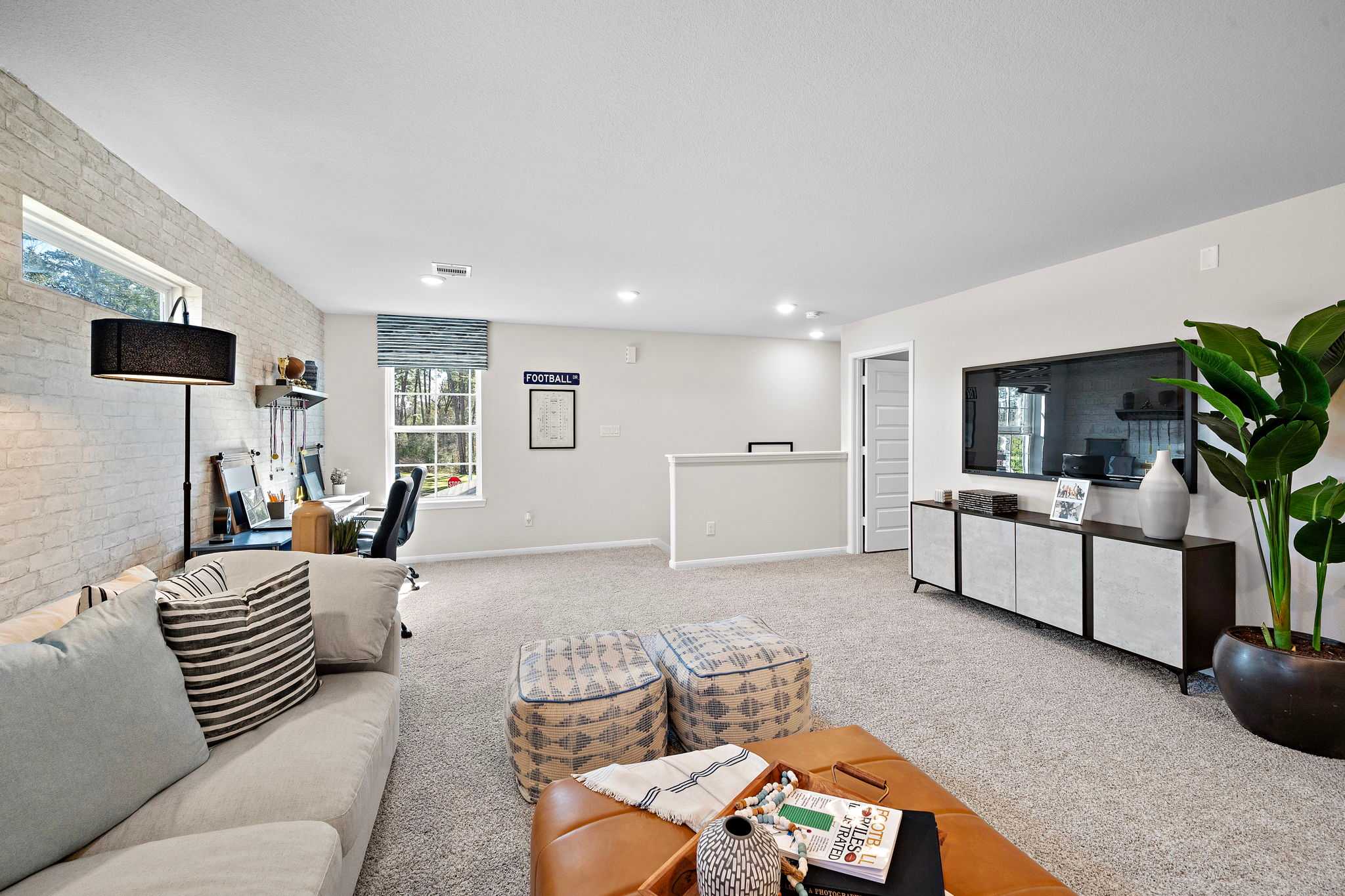 Cozy loft bonus room at Lakes at Black Oak in Magnolia TX with desk workspace, sofa, TV, and potted plants