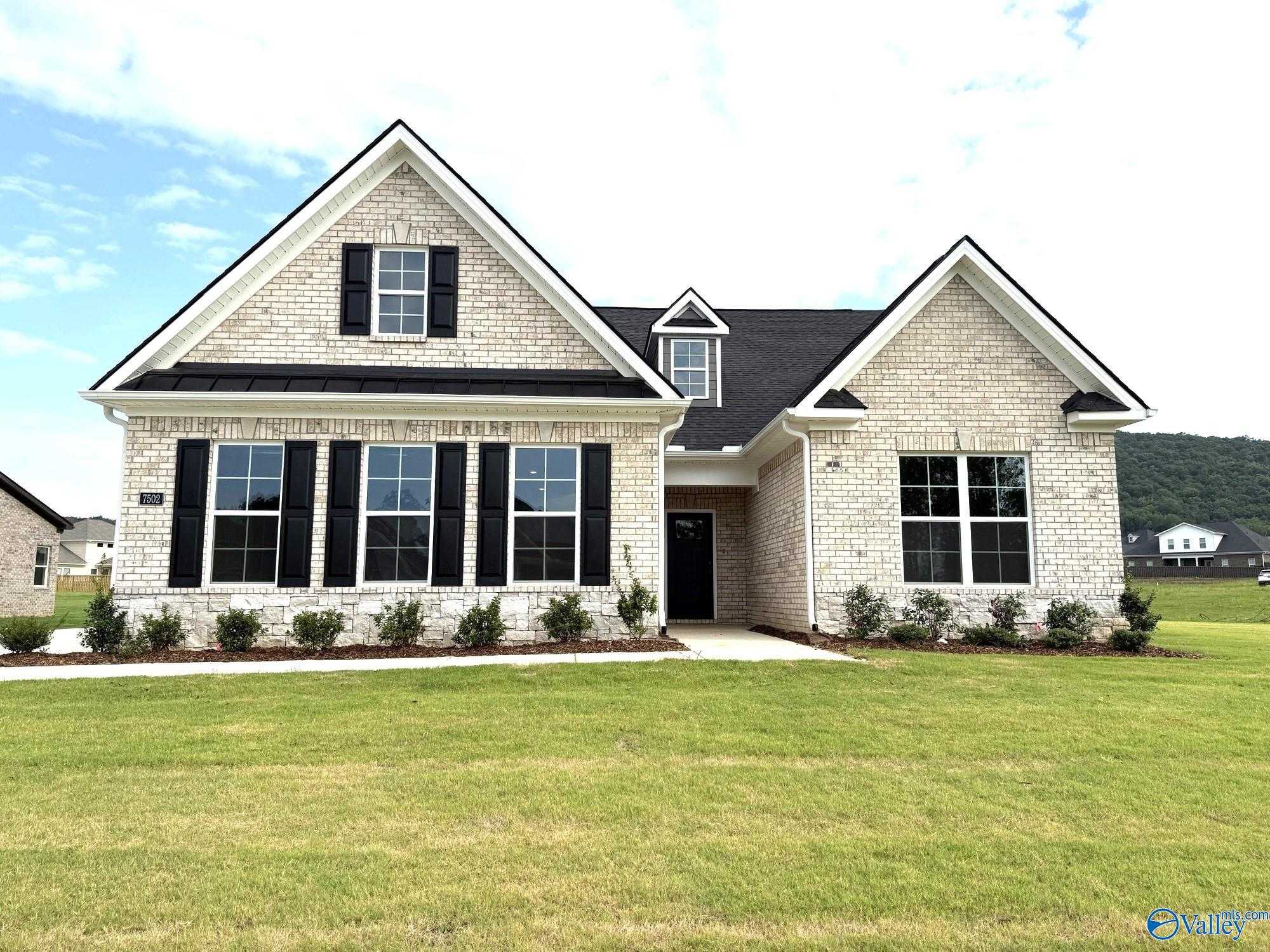 Modern 1.5-story tan brick home with black shutters, gabled roof, and landscaped front yard in The Meadows at Hampton Cove, Owens Cross Roads, Alabama - The Oxford by Evermore Homes