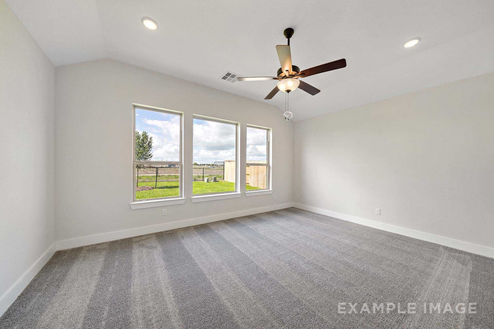 Spacious master bedroom in The Victoria A featuring vaulted ceiling, ceiling fan, triple windows with green backyard view, beige walls, gray carpet