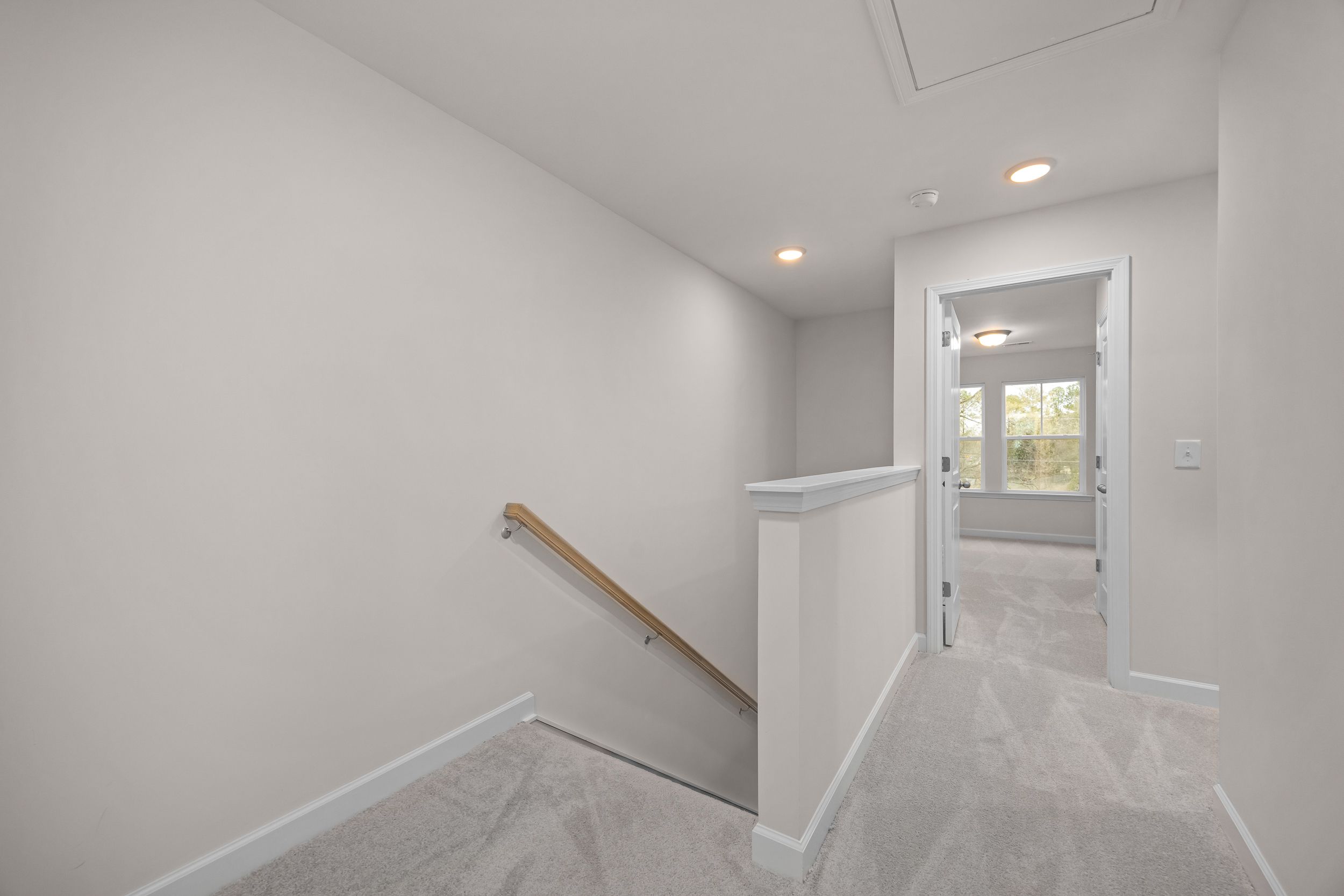 Bright upstairs hallway at Forestville Yard Townhomes in Knightdale NC with wooden staircase railing, white walls, and carpet flooring
