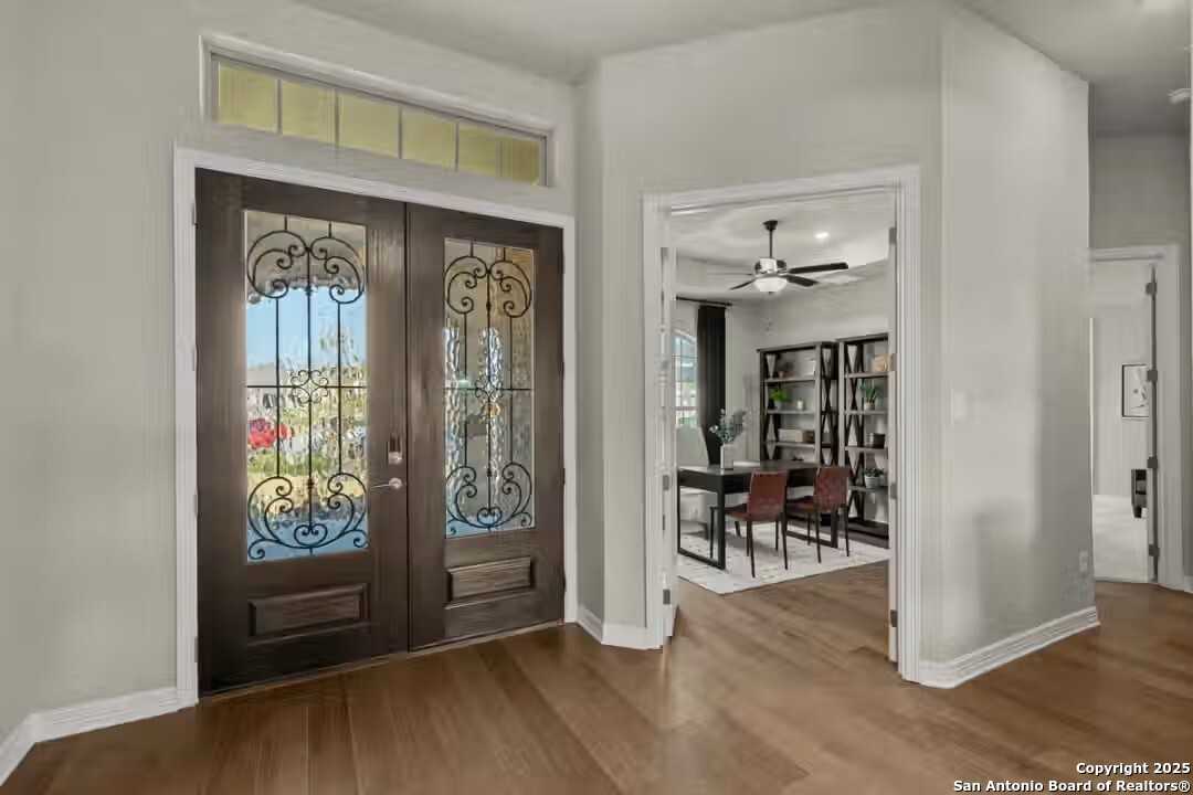 Elegant foyer with ornate wrought iron double doors, hardwood floors, and open dining area in Davidson Homes The Summerlin B, Castroville, Texas
