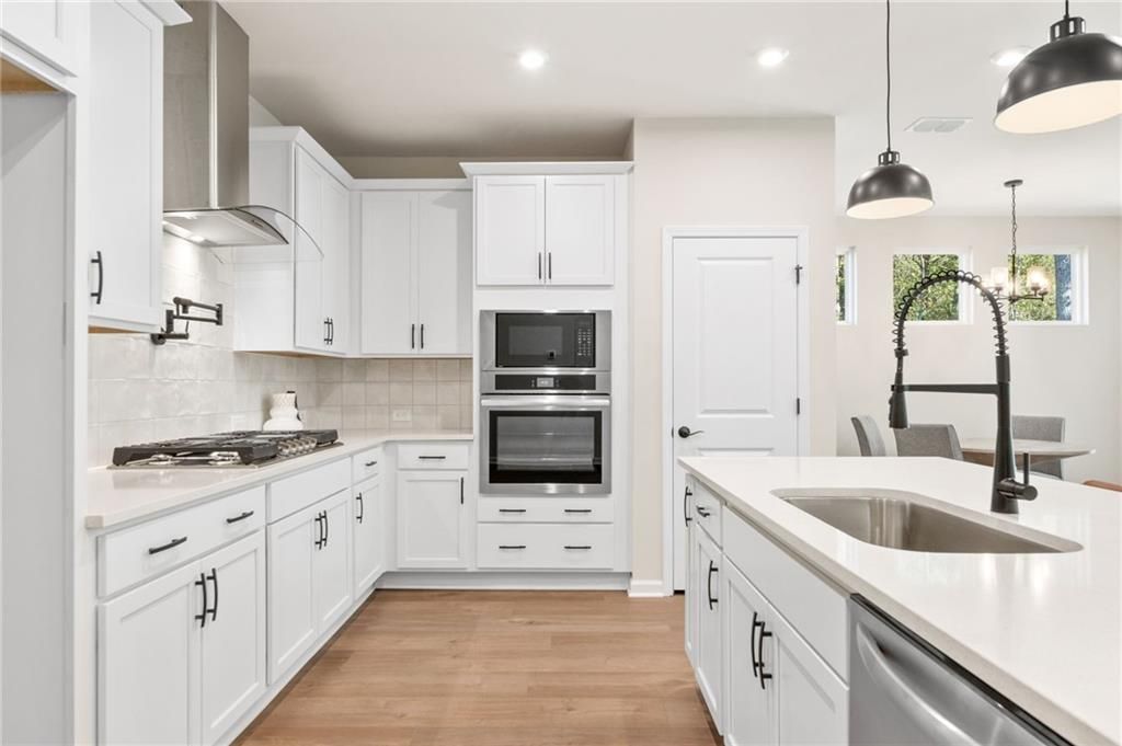 Modern white kitchen with island sink, double ovens, gas cooktop, and pendant lights in Davidson Homes The Daphne B, Loganville, GA