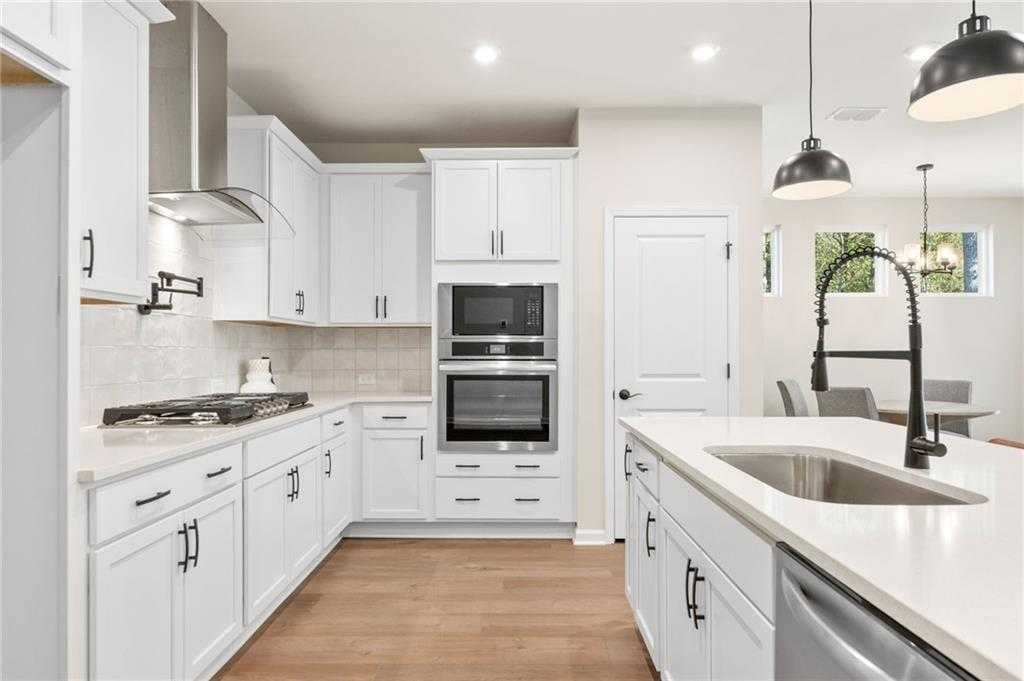 Modern white shaker kitchen with stainless double ovens, gas range, island sink, and pendant lights in Davidson Homes The Daphne B, Loganville, GA