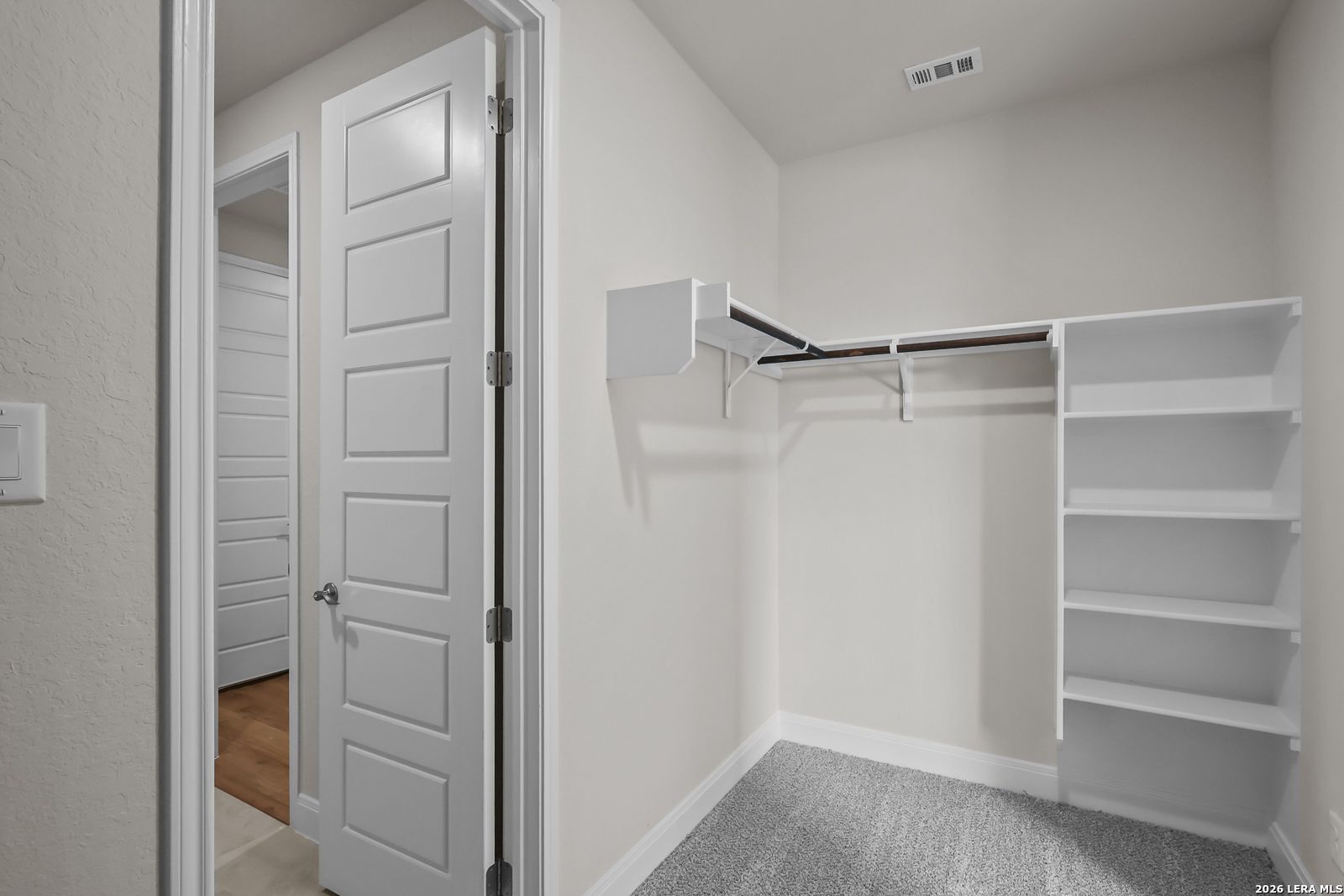 Walk-in closet with white shelving and neutral carpet in The Lanier H floor plan by Davidson Homes in Ladera, San Antonio.
