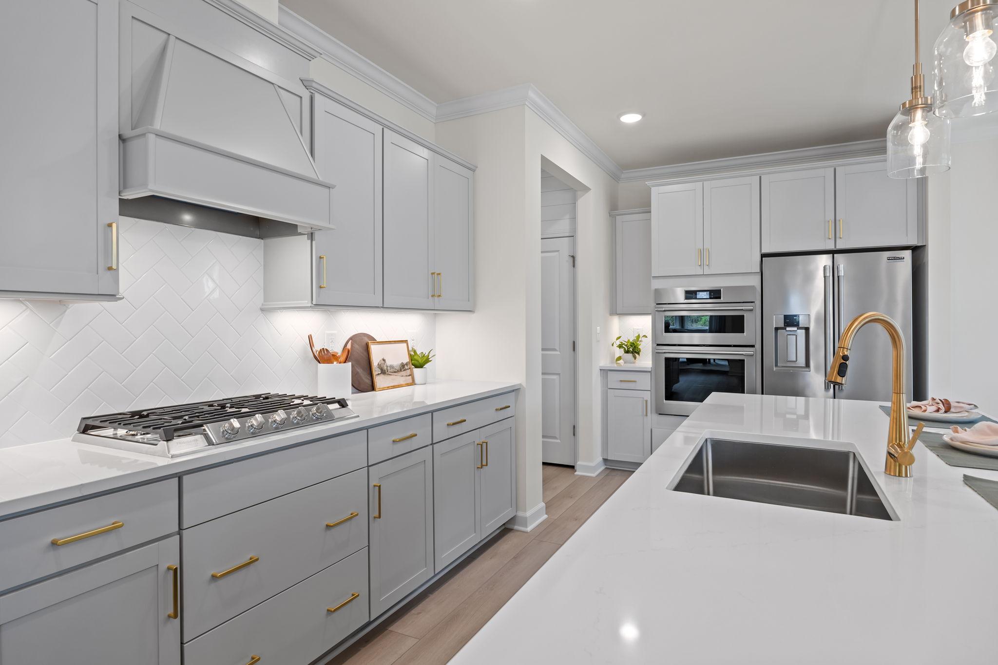 Modern kitchen in Springvale South by Davidson Homes featuring light gray cabinets, gold hardware, and white quartz counters.