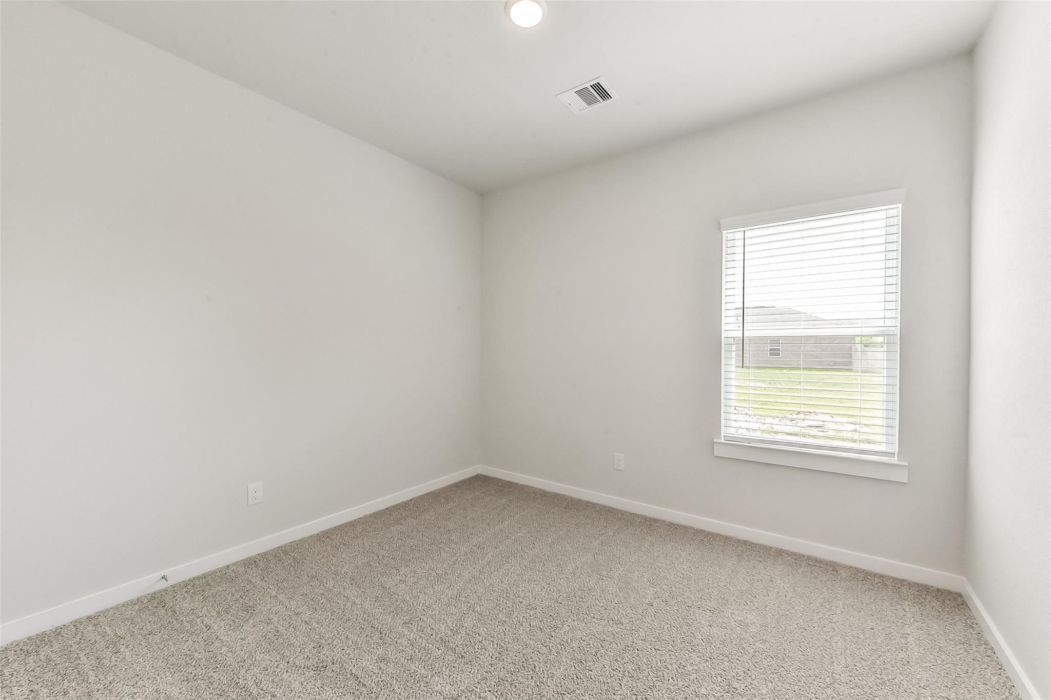 Empty bedroom with white walls, beige carpet, ceiling light, and window view of yard in Davidson Homes The Frio G, Magnolia, Texas