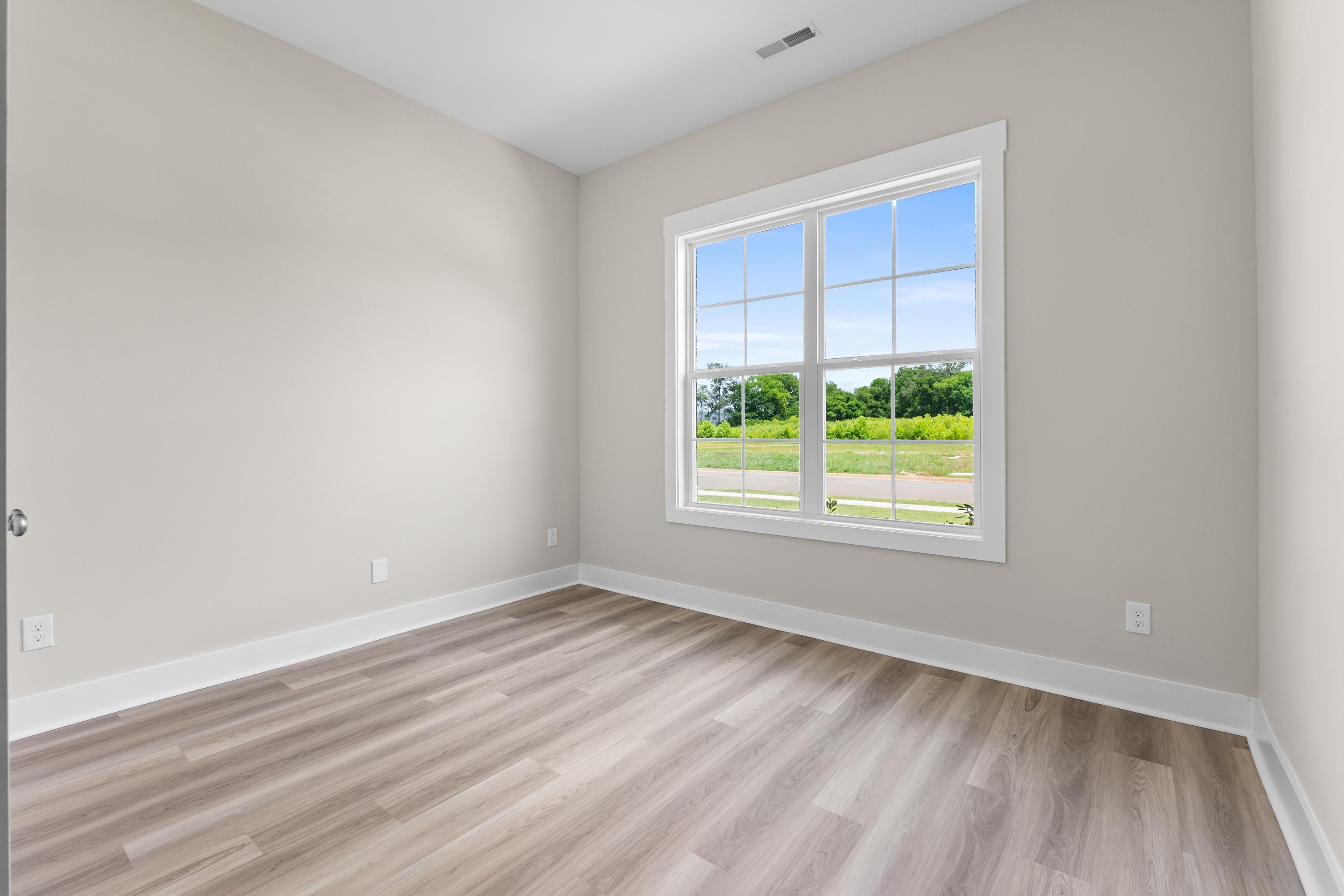 Spacious secondary bedroom in The Oxford A with light gray walls, large window overlooking green fields, and hardwood floors