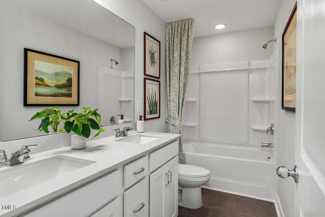 Elegant master bathroom with double vanity, framed art, potted plants, and soaking tub in Davidson Homes The Graham, Fuquay-Varina, NC