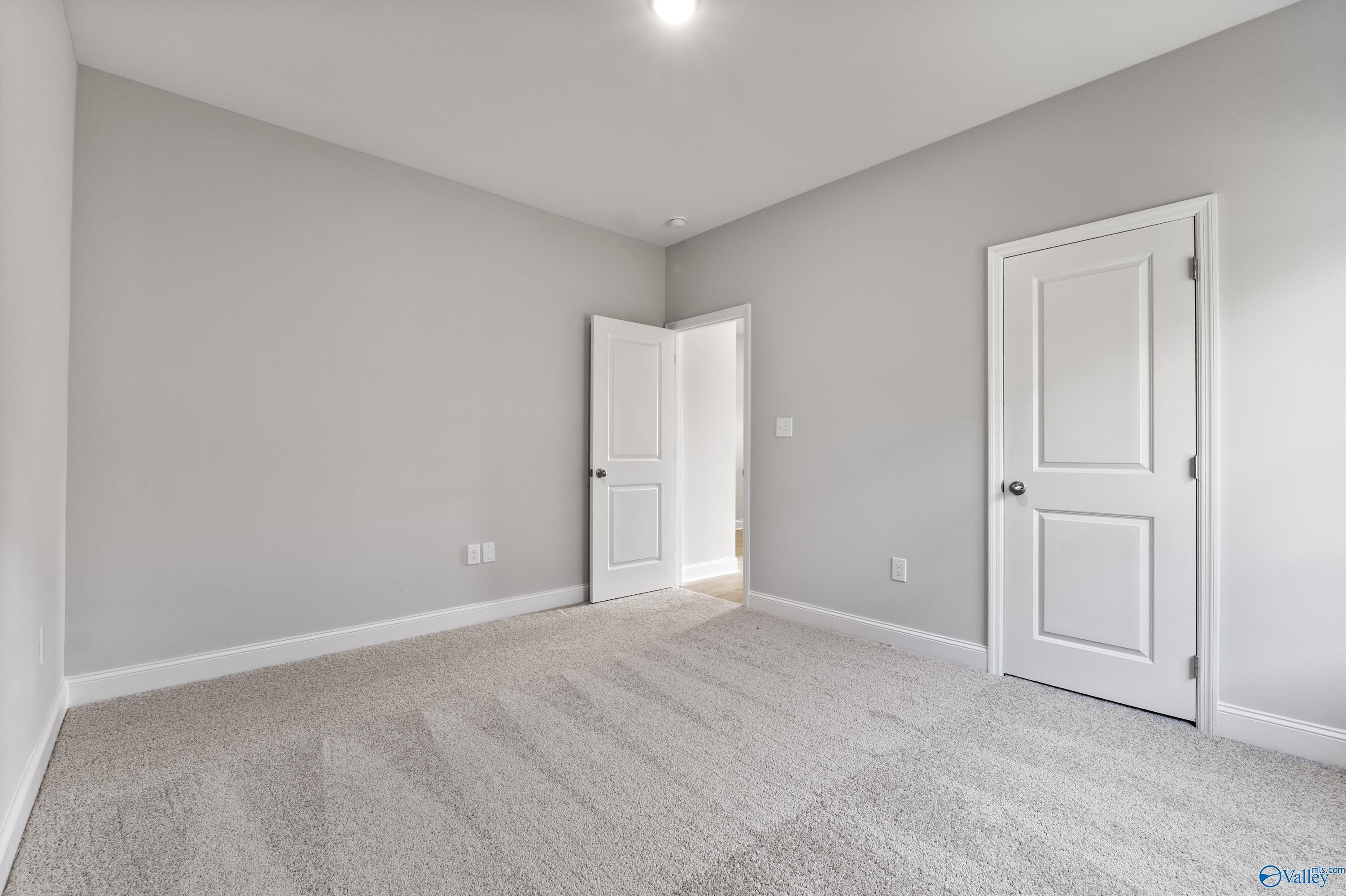 Empty bedroom featuring light gray walls, white doors, and beige carpet in Davidson Homes The Daphne C, Huntsville, Alabama