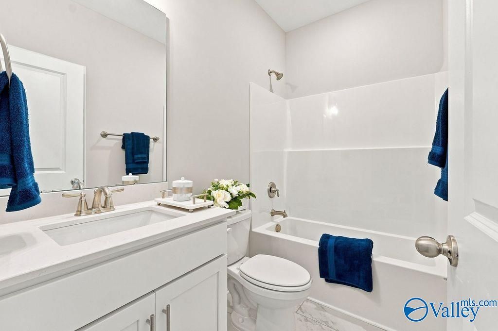 Bright white bathroom with tub-shower combo, navy towels, and double vanity in Davidson Homes The Harrison, Hartselle, Alabama