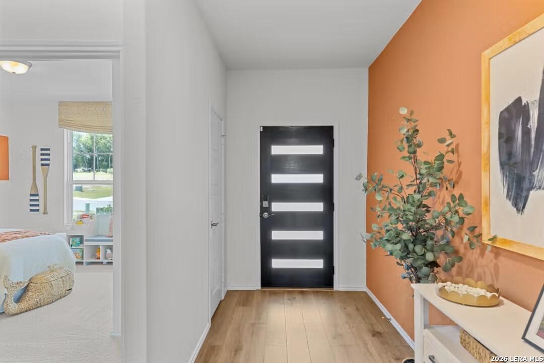 Modern hallway with orange accent wall, eucalyptus plant, abstract art, and coastal bedroom view in Davidson Homes The Daphne H, Seguin, Texas