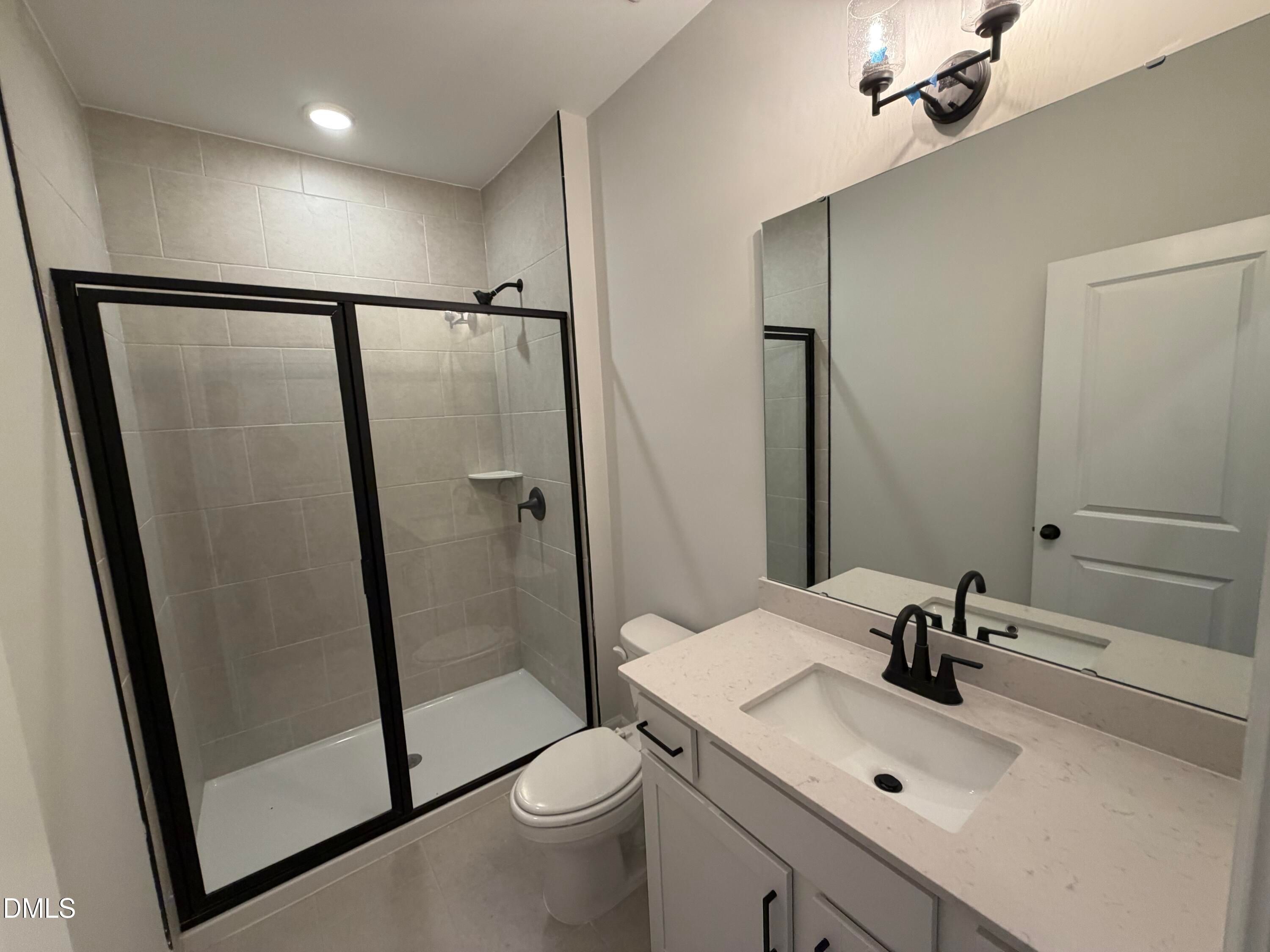 Modern bathroom with black-framed glass shower, white vanity, and matte black fixtures in Davidson Homes The Preston C, Wendell NC