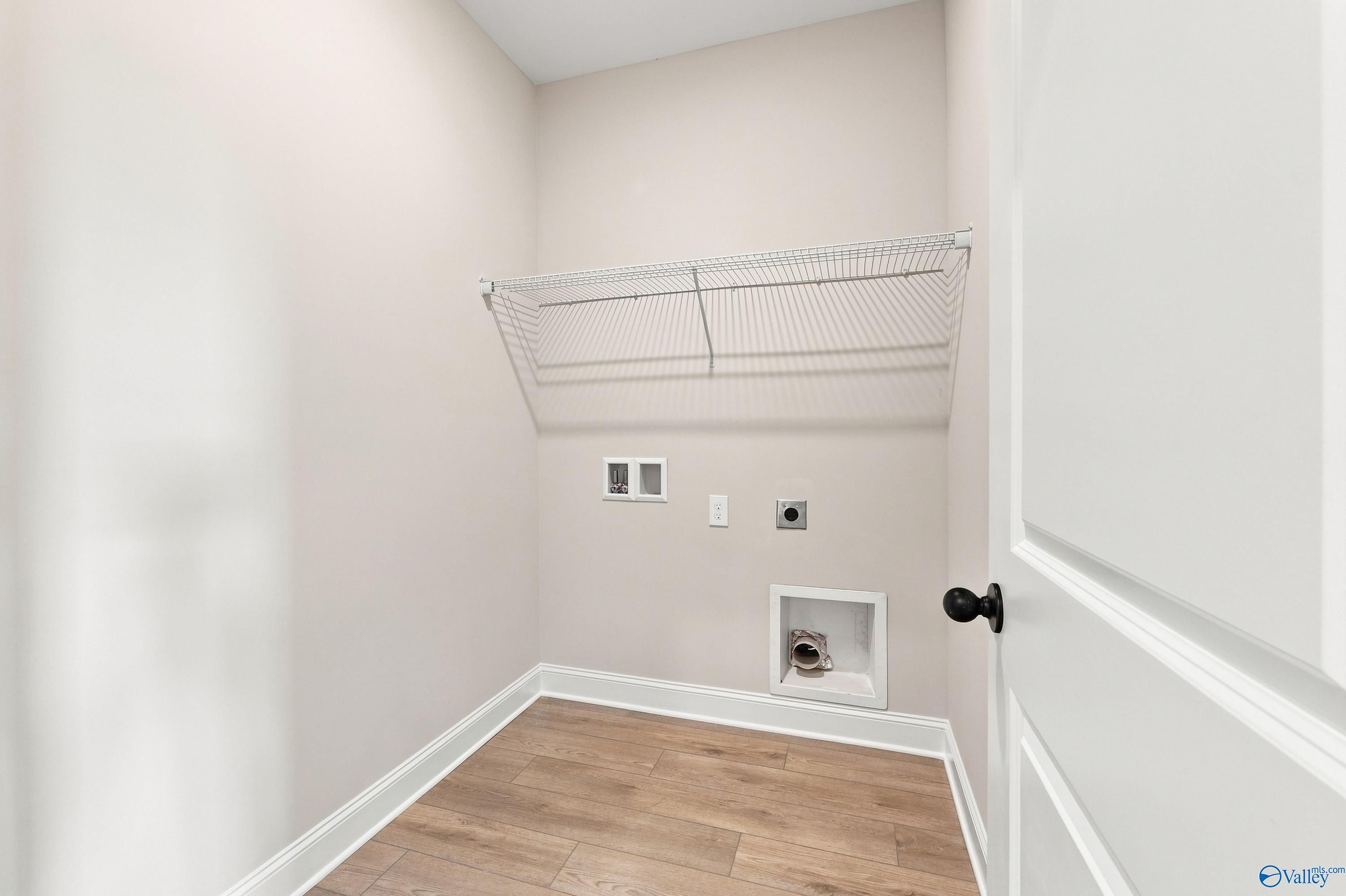 Laundry room with wire shelving, wood-look flooring, and washer connections in Davidson Homes Montgomery D, Athens, Alabama
