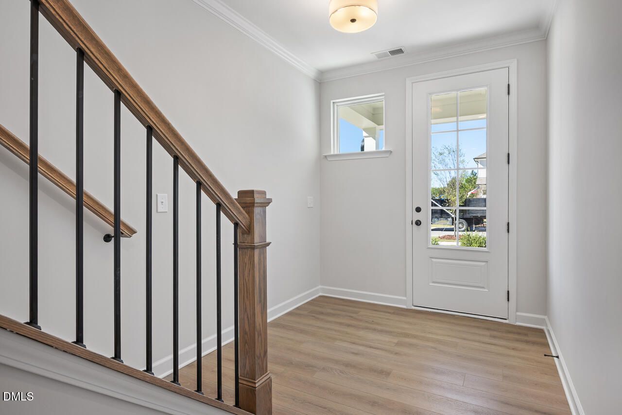 Bright foyer with glass-panel front door, wood-look flooring, and oak staircase with iron balusters in The Preston C, Wendell Ridge, NC