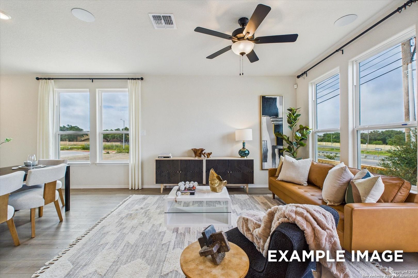 Bright living room with large windows, leather sofa, ceiling fans, and modern decor in The Florence C by Davidson Homes, San Antonio