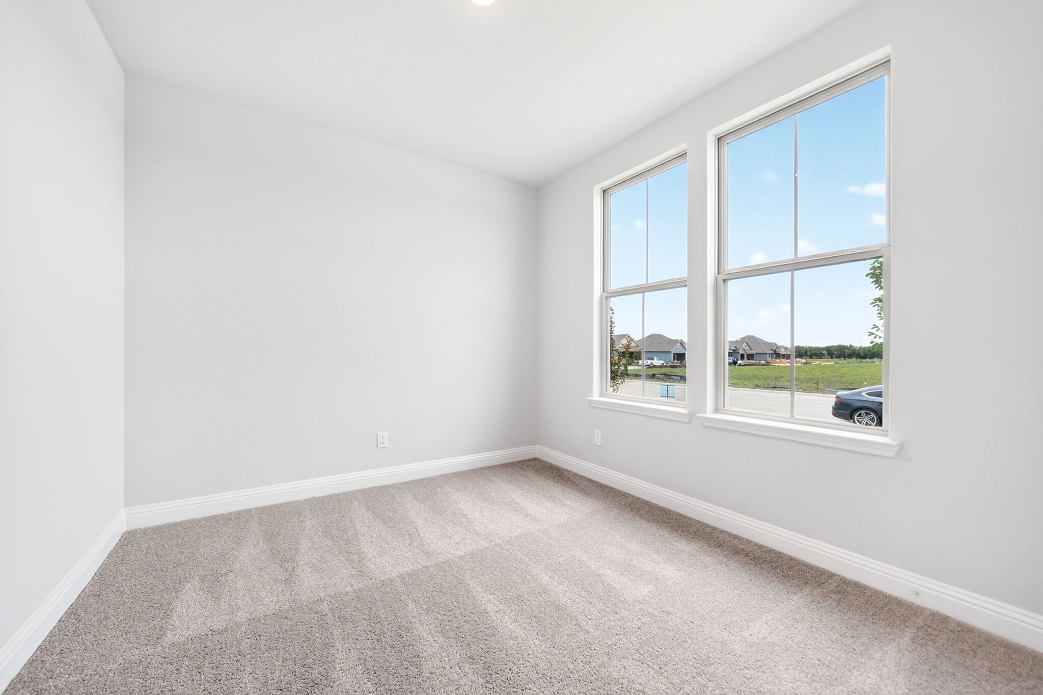 Bright, carpeted bedroom in The Redbud home design by Davidson Homes featuring large windows and neutral wall paint.