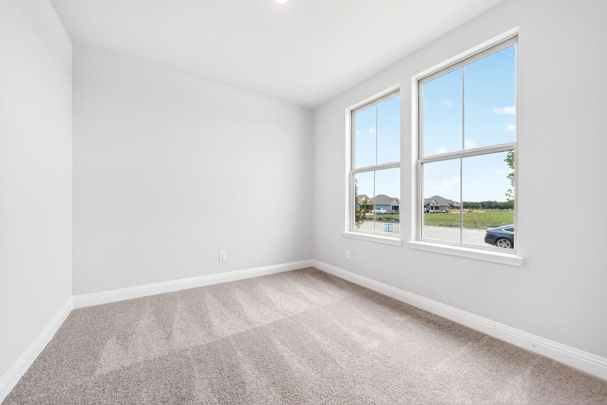 Bright, carpeted bedroom in The Redbud home design by Davidson Homes featuring large windows and neutral wall paint.