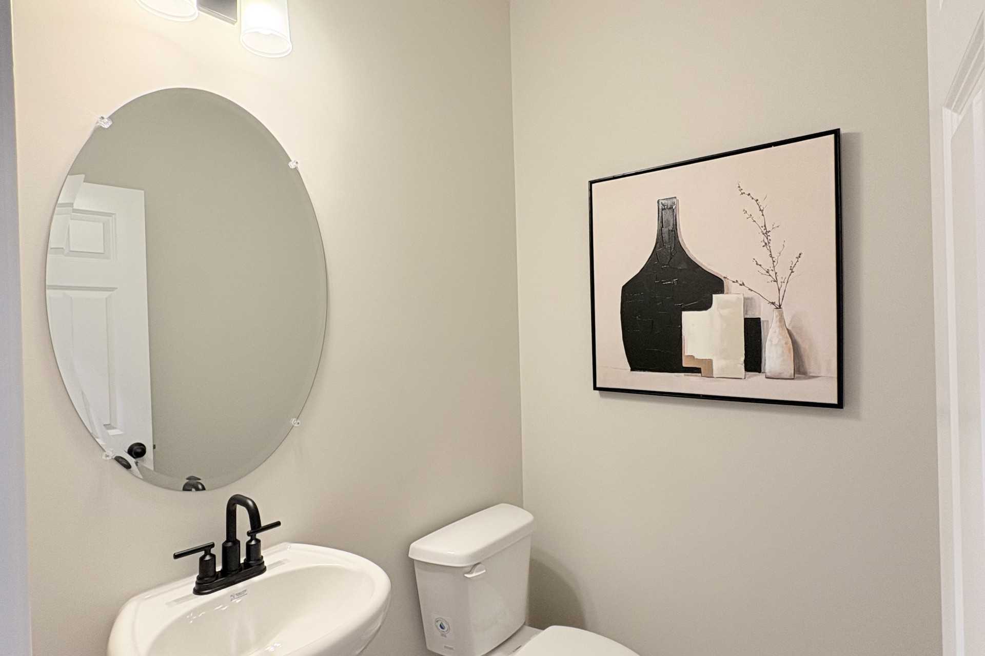 Elegant powder room in Hemingway community, Cumming GA by Davidson Homes featuring pedestal sink, round mirror and abstract art