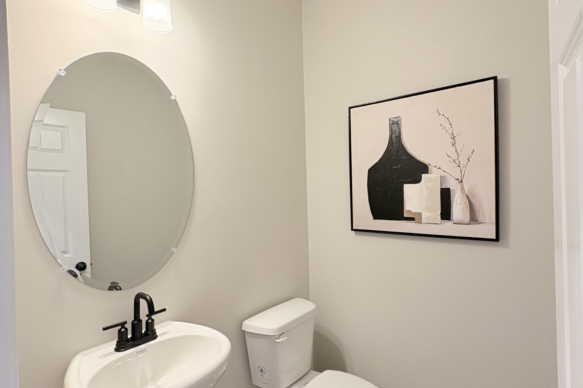 Elegant powder room in Hemingway community, Cumming GA by Davidson Homes featuring pedestal sink, round mirror and abstract art