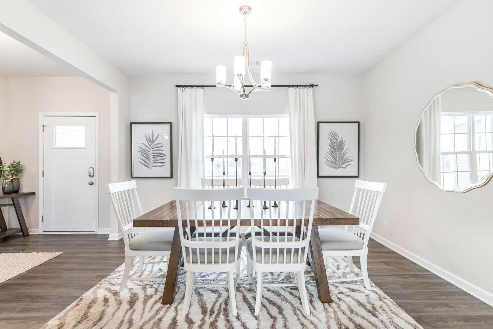 Elegant dining room in Cape Reserve at Donahue Ridge, Auburn AL featuring wooden table, white chairs, chandelier, and large window