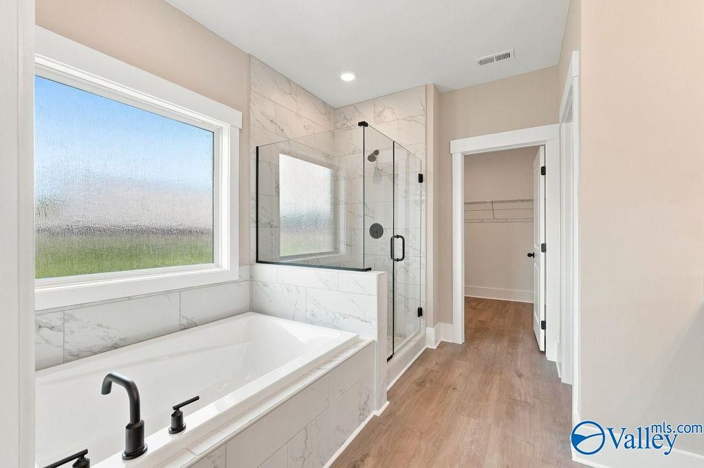 Modern master bathroom with soaking tub, glass-enclosed shower, and walk-in closet in The Rockford at Cain Park, Hartselle.