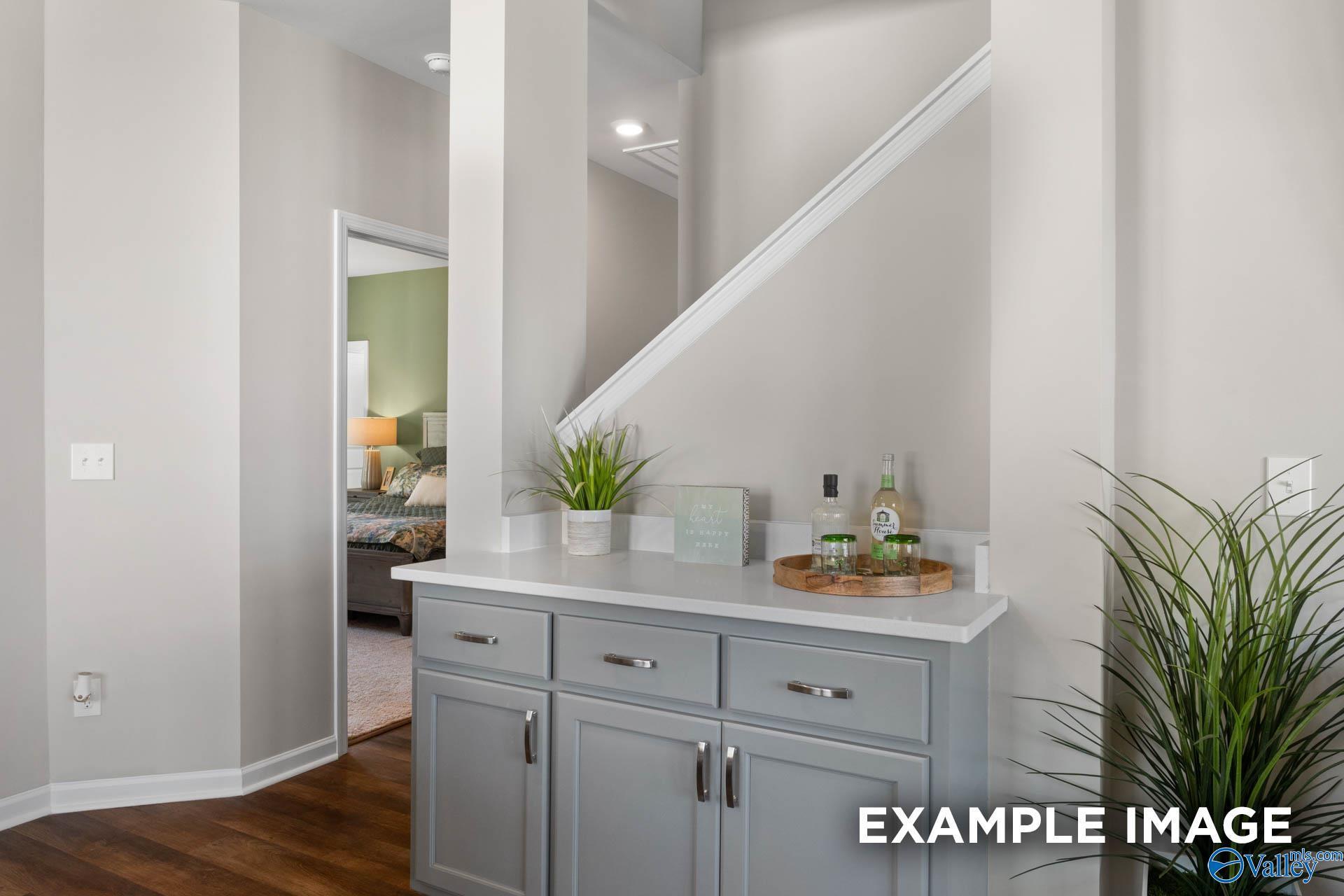 Elegant foyer staircase with gray console table, potted plants, and decor in Davidson Homes The Stella, Madison, Alabama