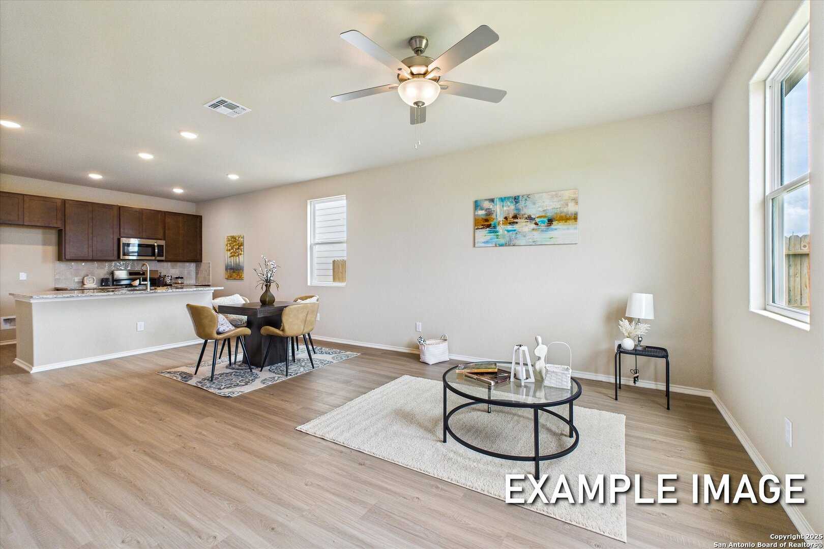 Modern open-concept living and dining area with wooden table, ceiling fan, abstract art, and kitchen in Davidson Homes The Comal B, Agave, San Antonio