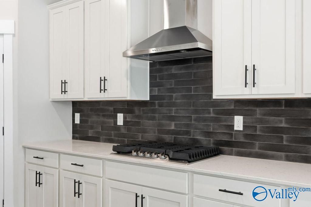 Modern white kitchen with shaker cabinets, black subway tile backsplash, stainless steel range hood and gas cooktop in Davidson Homes The Rockford, Hartselle, AL