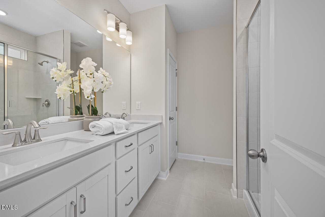 Elegant master bathroom with double vanity, white quartz counters, glass walk-in shower, and orchids in Davidson Homes The Carter C, Lillington NC
