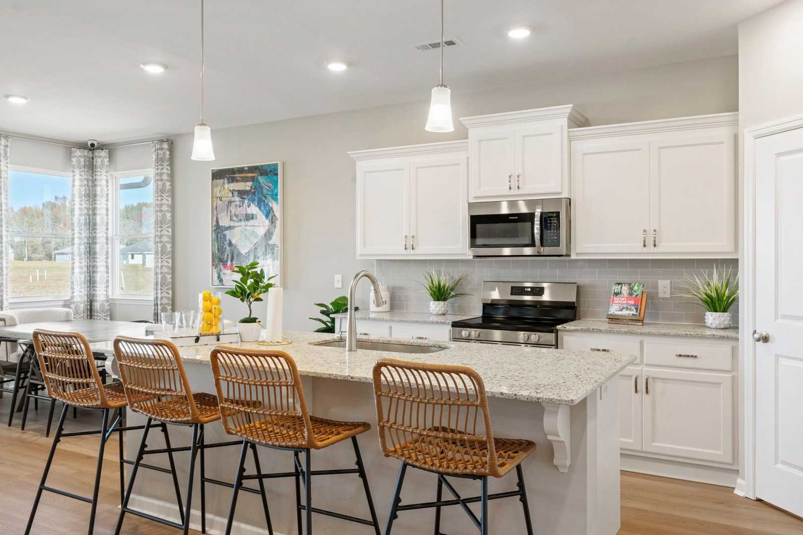 Spacious Phoenix home kitchen with white shaker cabinets, quartz island seating rattan barstools, stainless appliances, plants