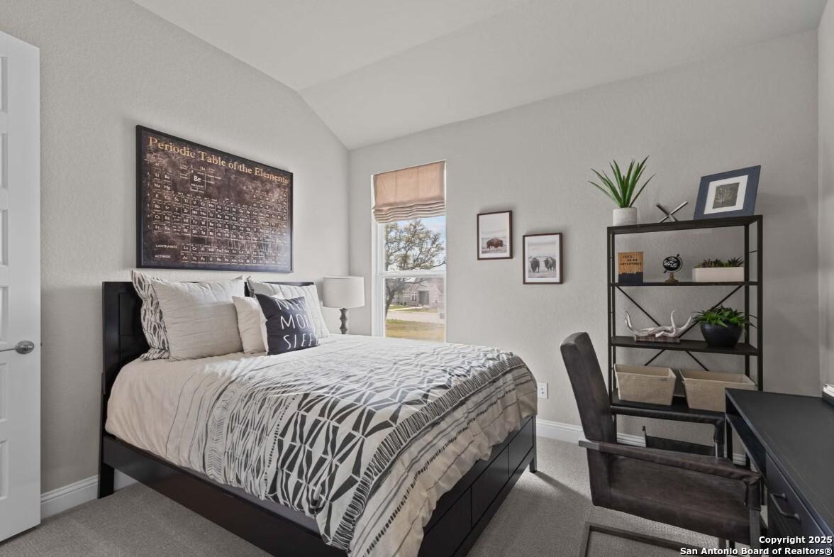 Cozy bedroom with neutral walls, patterned bedding on wood frame bed, bookshelf, desk, and window view in Davidson Homes The Garner B, Ladera, San Antonio