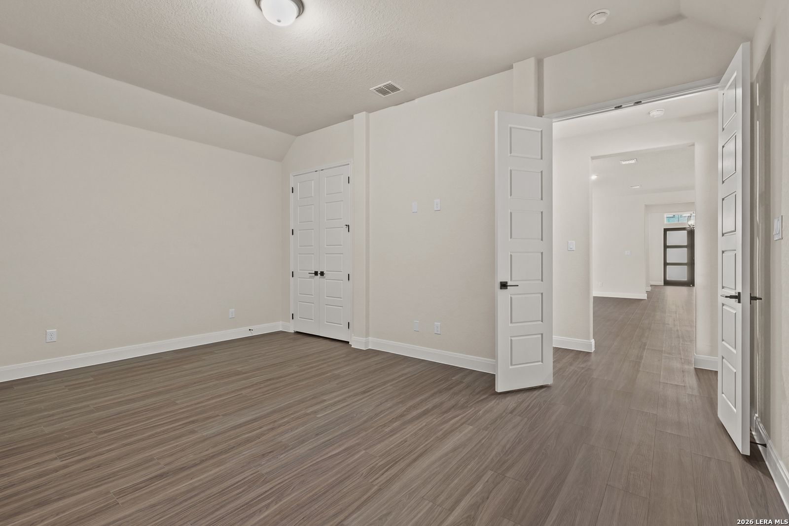 Spacious bedroom with wood-look tile floors and double doors in The Summerlin B floor plan at Potranco Oaks, Castroville.