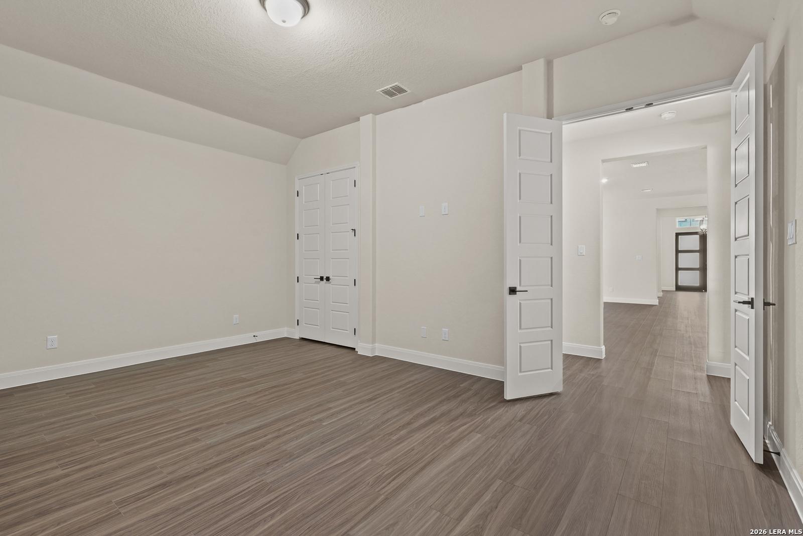 Spacious bedroom with wood-look tile floors and double doors in The Summerlin B floor plan at Potranco Oaks, Castroville.