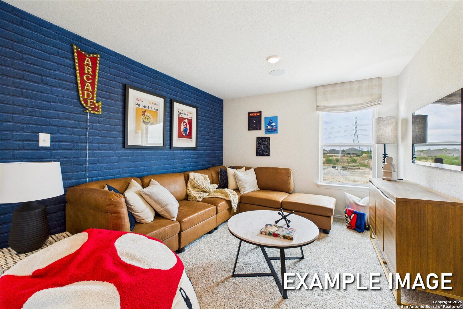 Cozy game room featuring navy blue brick accent wall, leather sectional sofa, arcade signage, and red bean bag in Davidson Homes The Brazos C, San Antonio