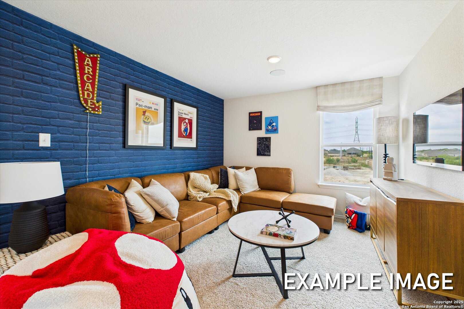 Cozy game room featuring navy blue brick accent wall, leather sectional sofa, arcade signage, and red bean bag in Davidson Homes The Brazos C, San Antonio
