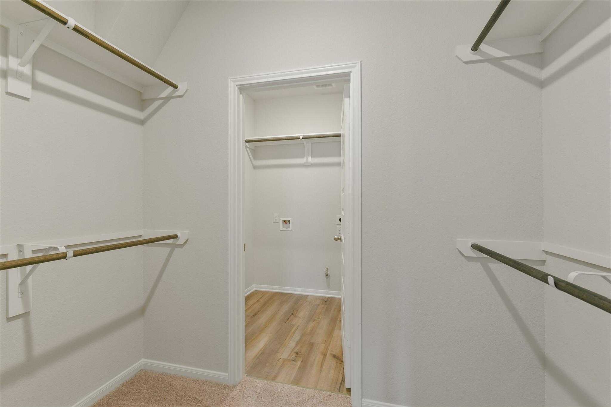 Spacious walk-in master closet with wood hanging rods, shelves, white walls, and laundry nook in Davidson Homes The Laguna B, Dayton TX